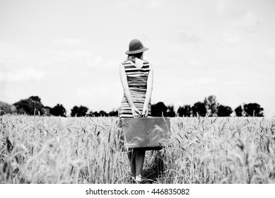 Black And White Photography Of Woman Wearing Hat Dress Holding Retro Suitcase Looking Away And Thinking Where To Go. Back View