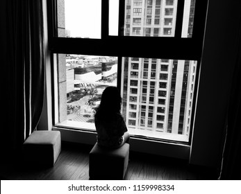 Black And White Picture Of Backside Of A Kid Sitting Alone And Looking Outside Through The Window. Homesick Or Sadness Or Broken Family Concept