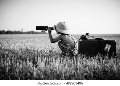 Black and white picture of boy wearing exciting looking in spyglass on outdoors field background. Little explorer with camera bag and old suitcase on sunny countryside. - Shutterstock ID 499203406