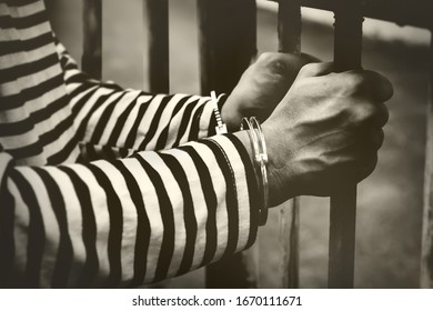 
Black and white picture Gesture of hopeless male prisoner : Illegal male prisoner hands were incarcerated and handcuffed inside the prison, using both hands to hold an old rusty iron cage, 
