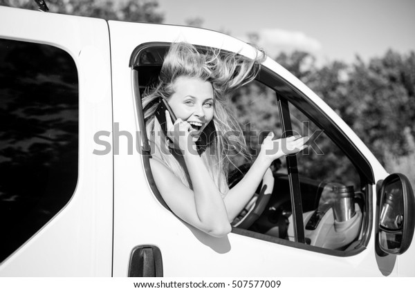 Black and white\
picture of joyful blond girl speaking phone and looking from car\
window. Young woman excited and smiling while talking with someone\
on sunny countryside\
background.
