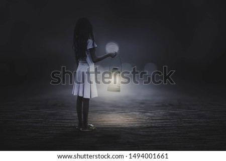 A black and white picture, a little girl holding a lantern in the street alone