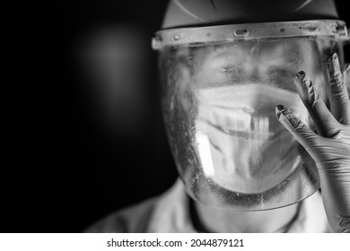 Black And White Picture Or Tired COVID Health Care Worker, Wearing A Mask, Face Shield, Gloves And Lab Coat.