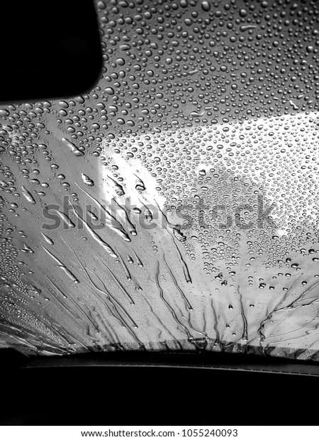 Black and white picture. Water droplets\
running off a foggy car\
windscreen.