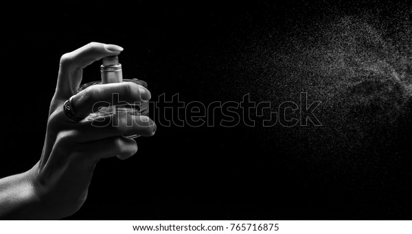 Black and white picture of woman push\
on perfume. Spray can with fume coming out on black background.\
Close up of a spray bottle drops on black\
background.