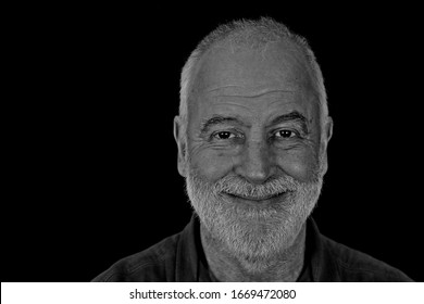 Black And White Portrait Of A 63 Year Old Man With Beard, Smiling Friendly Into The Camera.