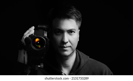 Black And White Portrait Of Asian Cameraman, Journalist, Reporter Holding Camcoder. Isolated On Black