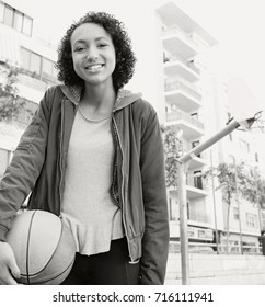 Black And White Portrait Of Beautiful African American Teenager College Student Girl In Basketball Court Holding Basket Ball, Looking Smiling Outdoors, Sports. Black Female Fitness Active Lifestyle.