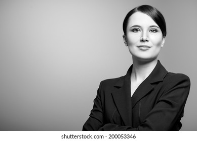 Black And White Portrait Of A Beautiful Elegant Professional Woman Standing With Folded Arms In A Stylish Jacket Looking At The Camera With An Enigmatic Smile, With Copy Space