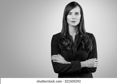 Black And White Portrait Of A Beautiful Elegant Professional Woman Standing With Folded Arms In A Stylish Jacket Looking At The Camera With An Enigmatic Smile, With Copy Space