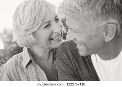 Black And White Portrait Of Beautiful Healthy Senior Couple Joyfully Smiling With Heads Together And Happy Expression, Outdoors. Mature People Enjoying Active Lifestyle, Closeness.