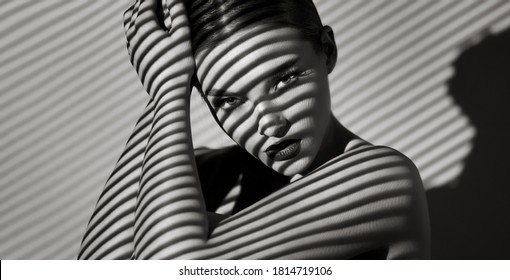 Black And White Portrait Of A Beautiful Young Woman With A Shadow Pattern On The Face And Body In The Form Of Stripes.