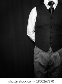 Black and White Portrait of Butler or Servant in Black Vest Standing With Hands Behind Back on Black Background. Service Industry. Copy Space for Text. Professional Hospitality and Courtesy.