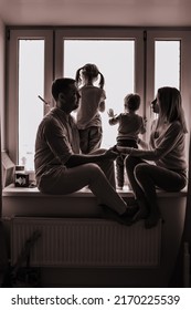 Black And White Portrait Of Caucasian Family Looking Out The Window. Little Boy And Girl Standing On Sill. Staying Home During Pandemia. Image With Selective Focus. High Quality Photo