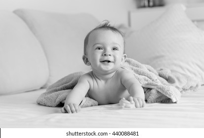 Black And White Portrait Of Cheerful Laughing Baby Boy Lying Under Blanket On Sofa