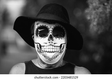 Black And White Portrait Of An Elderly Lady With A Catrina Mask And Hat, Celebrating Halloween And All Souls' Day, On The Street. Celebration, Costume, Party And Mask Concept.