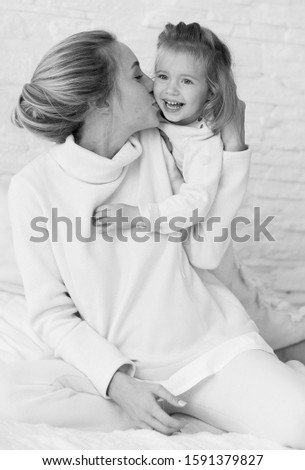 Black and white portrait emotional portrait of a happy and tender beautiful pregnant woman kissing her little daughter on the cheek while relaxing on the bed in the bedroom.Happy childhood.