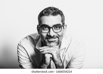 Black And White Portrait Of Handsome Man Wearing Blue Shirt And Glasses, Leaning On Hands, Posing On White Background