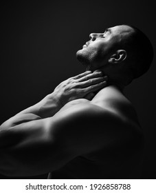 Black And White Portrait Handsome Sexy Muscular Man, Athlete With Perfect Built Body Standing Soide To Camera Holding Hand At Neck, Head Thrown Back And Eyes Closed Over Dark Background