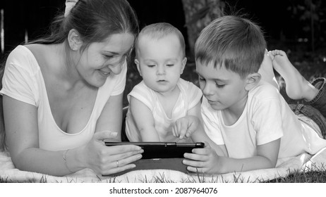 Black And White Portrait Of Happy Family With Children Relaxing In Park And Watching Video On Tablet Computer