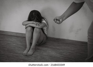 Black And White Portrait Of Little Afraid Girl Sitting With Knees Up, Crossed Arms, Covering Face. Man Stretching Hand With Fist To Beat. Protest Against Domestic Violence, Abuse, Fighting, Conflict.