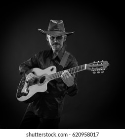 Black and white portrait of a man musician in black hat with guitar in hands playing and posing on black background in scenic light - Shutterstock ID 620958017