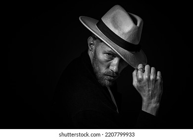 Black and white portrait of a mature gentleman with beard and moustache dressed in black coat and a hat. Dark key portrait on a black background. Male beauty. - Powered by Shutterstock
