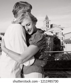 Black And White Portrait Of Mature Tourist Couple Hugging On Holiday Break, City Overview Romantic Vacation Together. Senior Man And Woman Travel, Sightseeing, Loving Leisure Recreation Lifestyle.