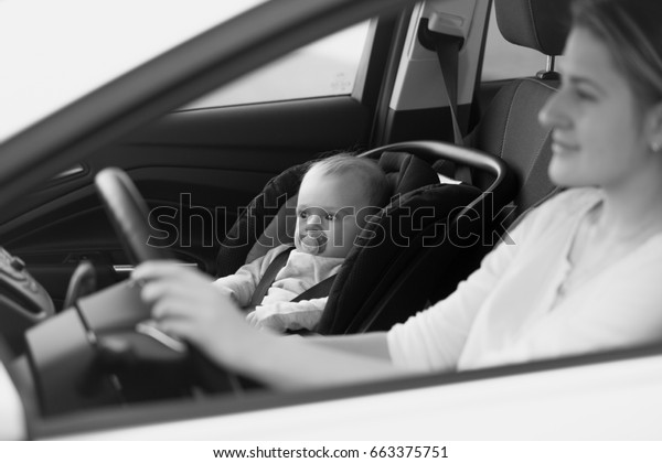 Black and white portrait of mother driving car\
with her baby sitting on front\
seat