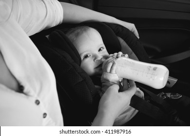 Black And White Portrait Of Mother Feeding Baby From Bottle In Car