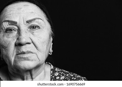 Black And White Portrait On An Old Woman On A Black Backgound. Sad Grandmother