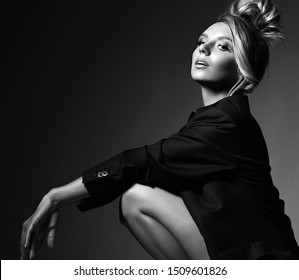 Black And White Portrait Of Self-confident Stylish Young Blonde Woman With Faux Hawk Mohawk In Formal Jacket Over Her Naked Body Sitting Squatting