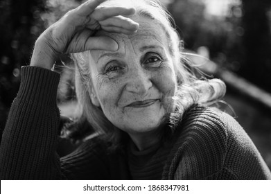 Black and white portrait of senior woman with grey hair and face with wrinkles outdoors relaxing at the park