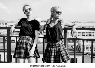  Black White Portrait Portrait Of Two Pretty Hipster Blonde Sisters  Wearing Plaid Skirt And  Black T-shirt. Girls Smile, Have Fun Against  Urban City.