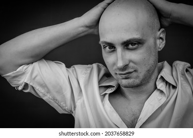 Black And White Portrait Of A Young Bald Man In A Shirt With His Hands Behind His Head And A Provocative Look