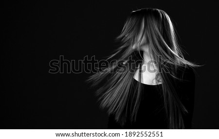 Black and white portrait of young happy brunette woman with luxurious long hair shaking her head to make her hair flying in the wind after hair restoring spa procedures. Hairstyle. Hair cosmetics