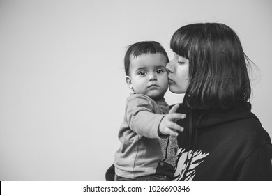 Black And White Portrait Of Young Mother Who Is Kissing Her Son, Toddler With Serious Sad Expression, Lots Of Place For Text 