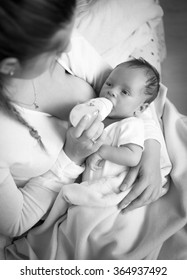 Black And White Portrait Of Young Mother Feeding Baby With Milk From Bottle