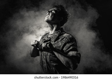 Black white portrait of a young soldier in combat coloring, scars and bruises, holding a machete on a black background with smoke