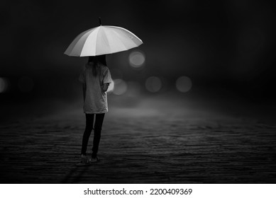 A Black And White Portrait Of A Young Woman Walking With An Umbrella On The Streets Alone At Night.