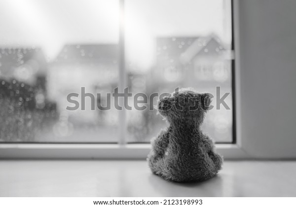 Black and white Rear view Lonely bear doll sitting\
alone looking out of window, Sad teddy bear sitting next to window\
in rainy day, lost toy, Loneliness concept, International missing\
Children day