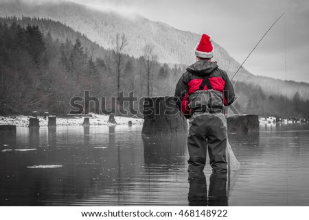 Black, White & Red Photo of a Man Fly Fishing in a Christmas Santa Hat - Wearing a Red Jacket and Waders, with Trees and Mountains in the Background in the Pacific Northwest on a Cloudy Winter Day