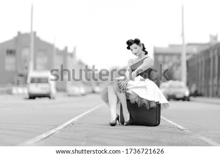 Black and white retro style photo. A girl in a dress and hairstyle in the style of the 40-50s on a city street on tram tracks on a sunny day