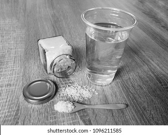 Black And White Salt In The Spoon And Glass Bottle With Water On Wooden Table.