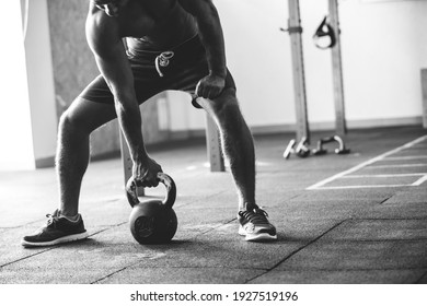 Black and white shot of an athlete with a bare torso. Athletic built man doing kettlebell exercise