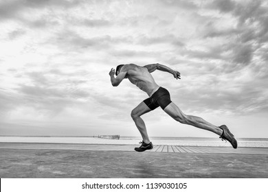 Black & White shot of a handsome muscular caucasian white European male in  full sprint with a beach and dramatic sky background