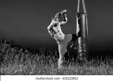 Black and white shot of a kick boxer training on a heavy bag outdoors kicking it with his knee copyspace kickboxing martial arts combat fighting practicing performance concentration determination. - Powered by Shutterstock