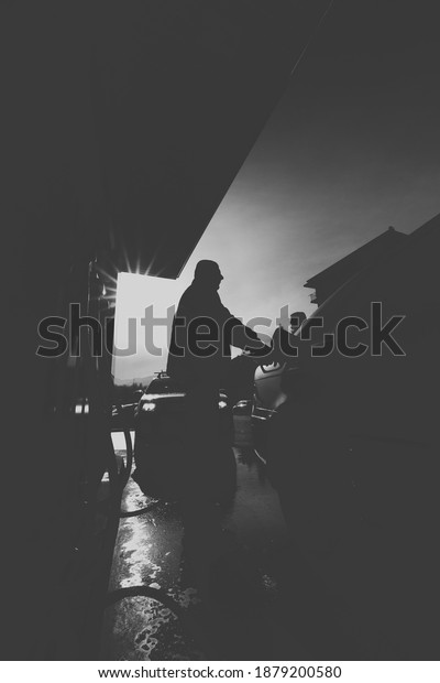A black and white shot of a person\
filling up their car with petrol at the gas\
station