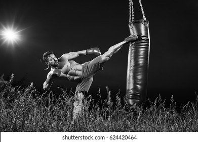 Black and white shot of a professional kick boxer practicing on a heavy punching bag outdoors at night copyspace motivation lifestyle workout muscles power strength masculinity martial sportsperson. - Powered by Shutterstock