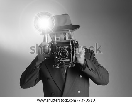 Black & White shot of a retro 1940's stylephotographer wearing a Fedora hat and holding a vintage camera with flash bulb flashing